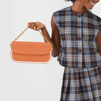 Orange shoulder bag worn with gold chain strap and white handle accents