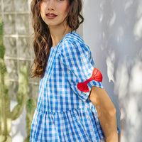 Blue gingham blouse with short puff sleeves and red ribbon bow accents at the cuff