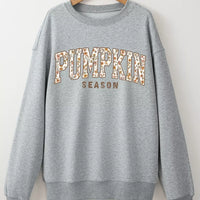 Gray oversized pullover sweatshirt hanging on a hanger, “PUMPKIN SEASON” chest graphic