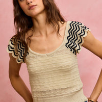Oatmeal knit tank top with wavy texture, flutter sleeves, and black zigzag trim