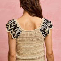 Back of oatmeal knit top with wavy texture and black zigzag flutter sleeves