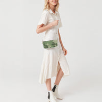 Green camouflage crossbody shoulder bag with flap front and white strap, worn over dress.