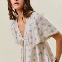 Ivory blouse with blue dot print, V-neck tie front, and layered flutter sleeves.