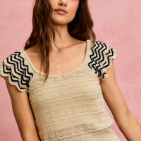 Oatmeal textured knit top with scalloped flutter sleeves and black zigzag trim