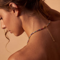 Gold tennis necklace with rainbow CZ stones on model’s neck and shoulder