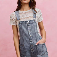 Light wash denim overall romper with adjustable straps, front buttons, and patch pockets