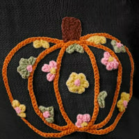 Black knit sweater close-up: orange stitched pumpkin with colorful flower embroidery