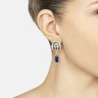 Gold art deco drop earrings on ear, with blue sapphire teardrop and crystal arch