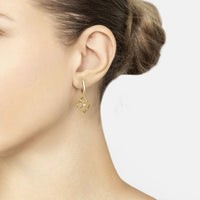 Gold clover drop earrings with crystal centers, worn on model’s ear