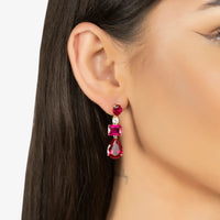 Gold drop earrings with ruby-red stones, worn on model with dark hair side view