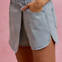 Washed light blue denim wrap skort with button closure and curved front overlay