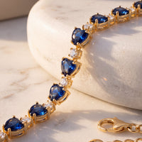 Gold-tone tennis bracelet close-up with blue faceted stones and heart charms
