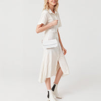 White mini shoulder bag with gold chain strap and flap, worn crossbody.