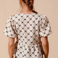 Back view of ivory woven peplum top with black ribbon bows and short puff sleeves.