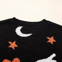 Black sweater close-up showing moon, orange star bursts, and pumpkin graphic on knit