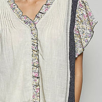 Cream V-neck blouse close-up with floral ruffle trim and textured placket