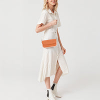 Orange shoulder bag on model with white dress and gold chain strap detail