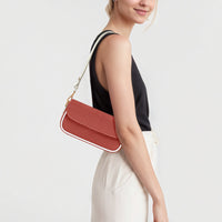Red leather shoulder bag worn over white outfit, front flap and gold chain strap
