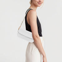 White mini shoulder bag worn at shoulder with gold chain strap and flap.