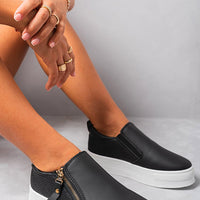 Black slip-on trainers with side zipper detail, gold-tone accents, and cushioned collar