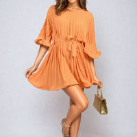 Orange pleated mini dress with tie waist and wide sleeves, flowing A-line skirt.