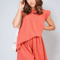 Coral sleeveless ruffle-trim top and matching tiered shorts set, front close-up.