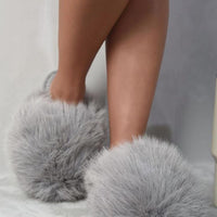 Grey faux fur open-back slippers with fluffy upper and flat sole on bare feet