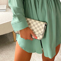 Light check clutch bag with front flap and gold chain strap, held in hand