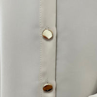 Beige button placket close-up with round gold-tone buttons and vertical stitching
