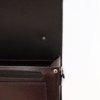 Dark leather bag close-up with zipper pocket and metal rivets on front panel