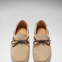 Pair of taupe suede driving loafers viewed from above, with dark bow laces and stitched toes