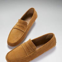 Pair of tan suede penny driving loafers, shown at an angle with stitched apron toes.