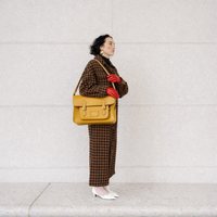 Yellow ochre leather satchel worn crossbody with flap closure and front buckle details