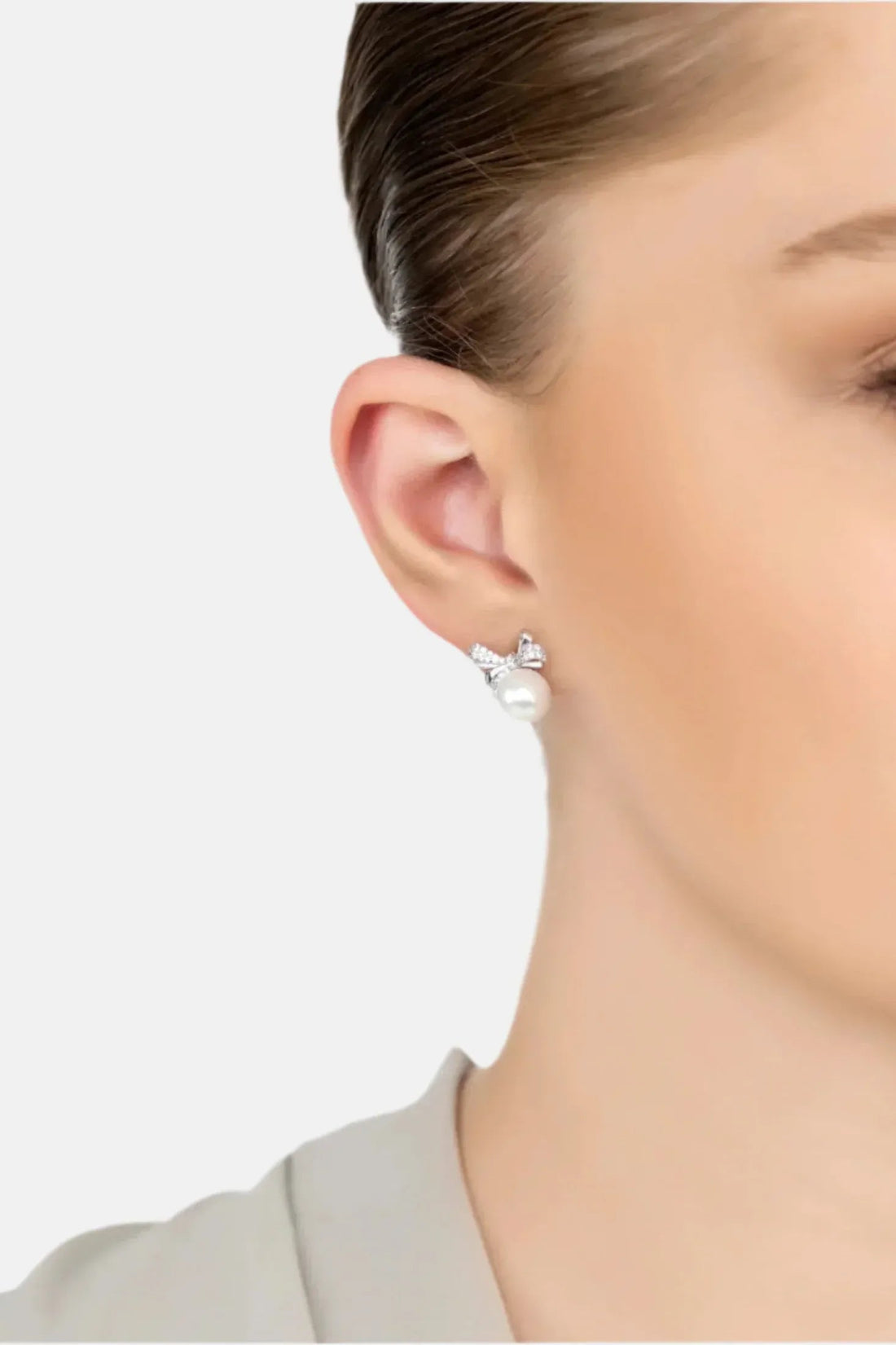 Silver stud earrings with bow ribbon and round white pearl worn on ear