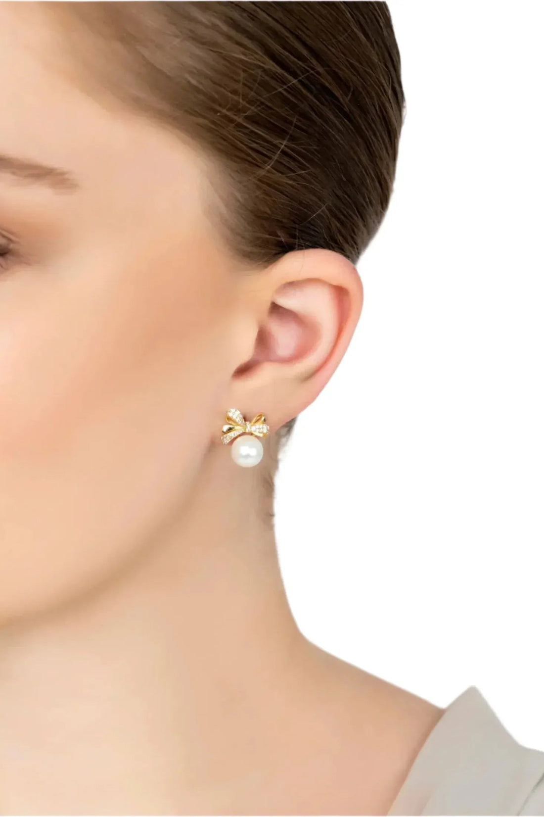 Gold ribbon bow pearl stud earrings on model ear with small crystal bow and pearl