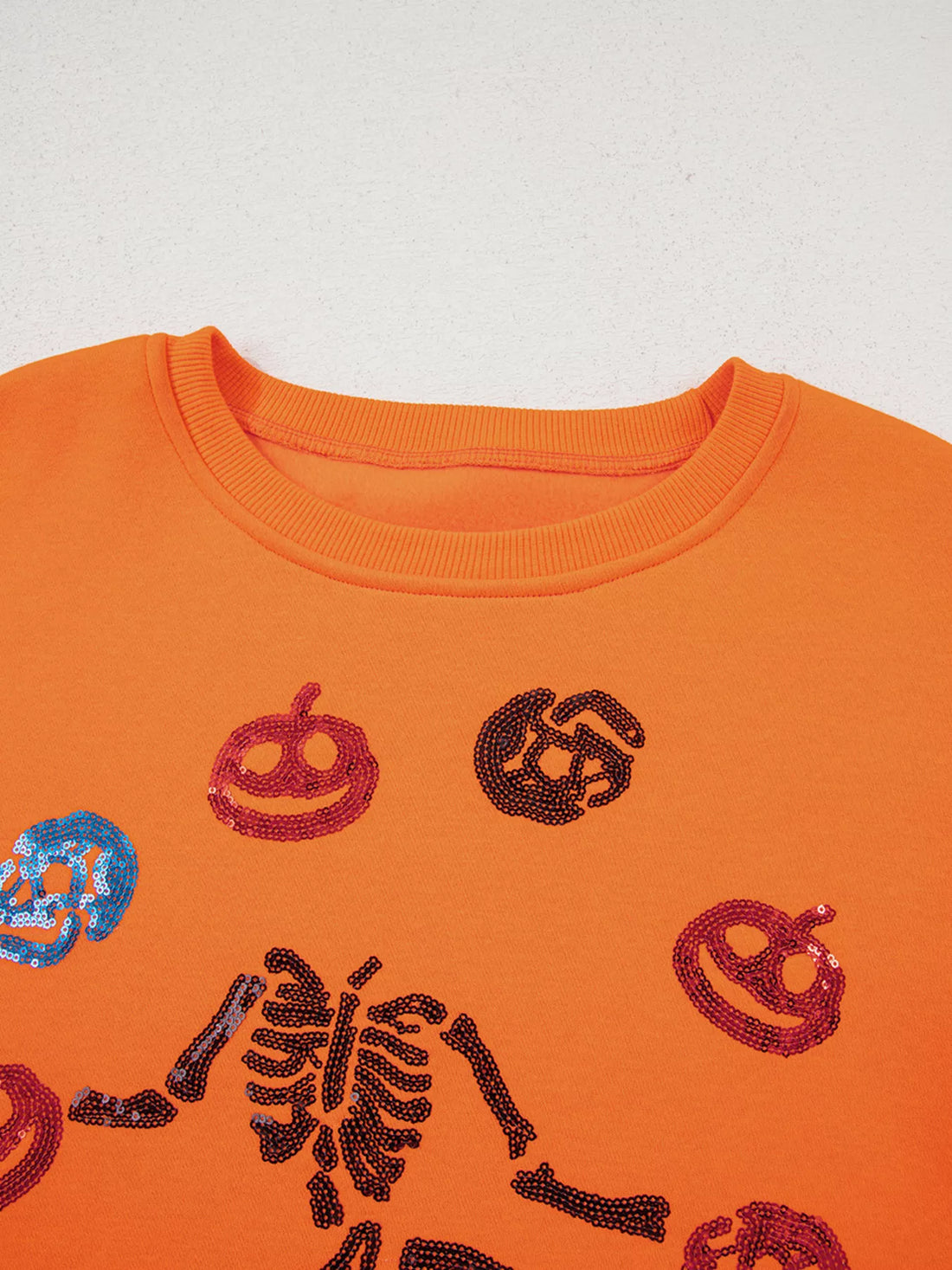 Orange crewneck sweatshirt close-up: sequin critter icons near ribbed neckline