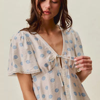 Ivory blouse with blue circular dot print, tie-front V-neck, and flutter sleeves.