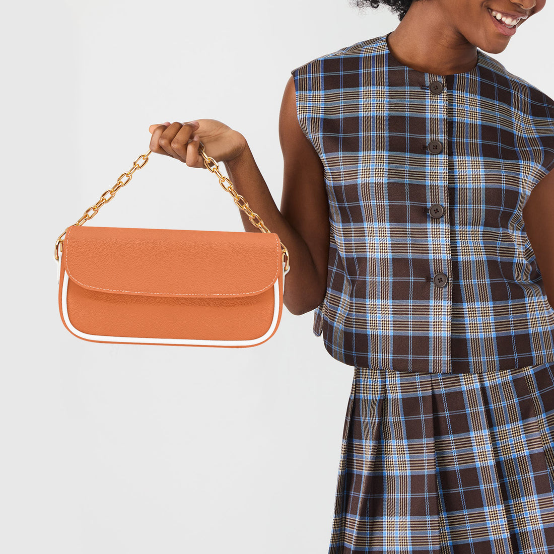 Orange shoulder bag worn with gold chain strap and white handle accents