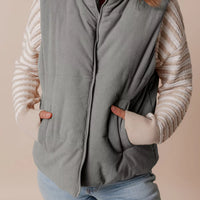 Gray corduroy stand-neck puffer vest with full-length front zipper and ribbed texture.