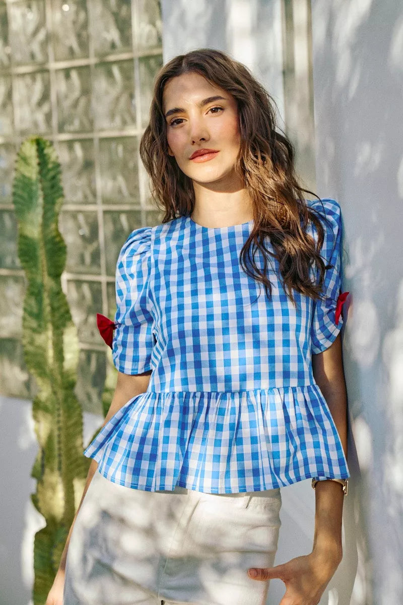 Blue gingham peplum blouse with flutter sleeves and red bow accents at the shoulders