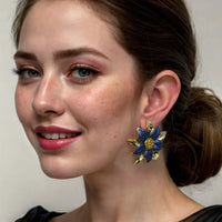 Blue daisy flower stud earrings with gold-tone backing, worn by a model.