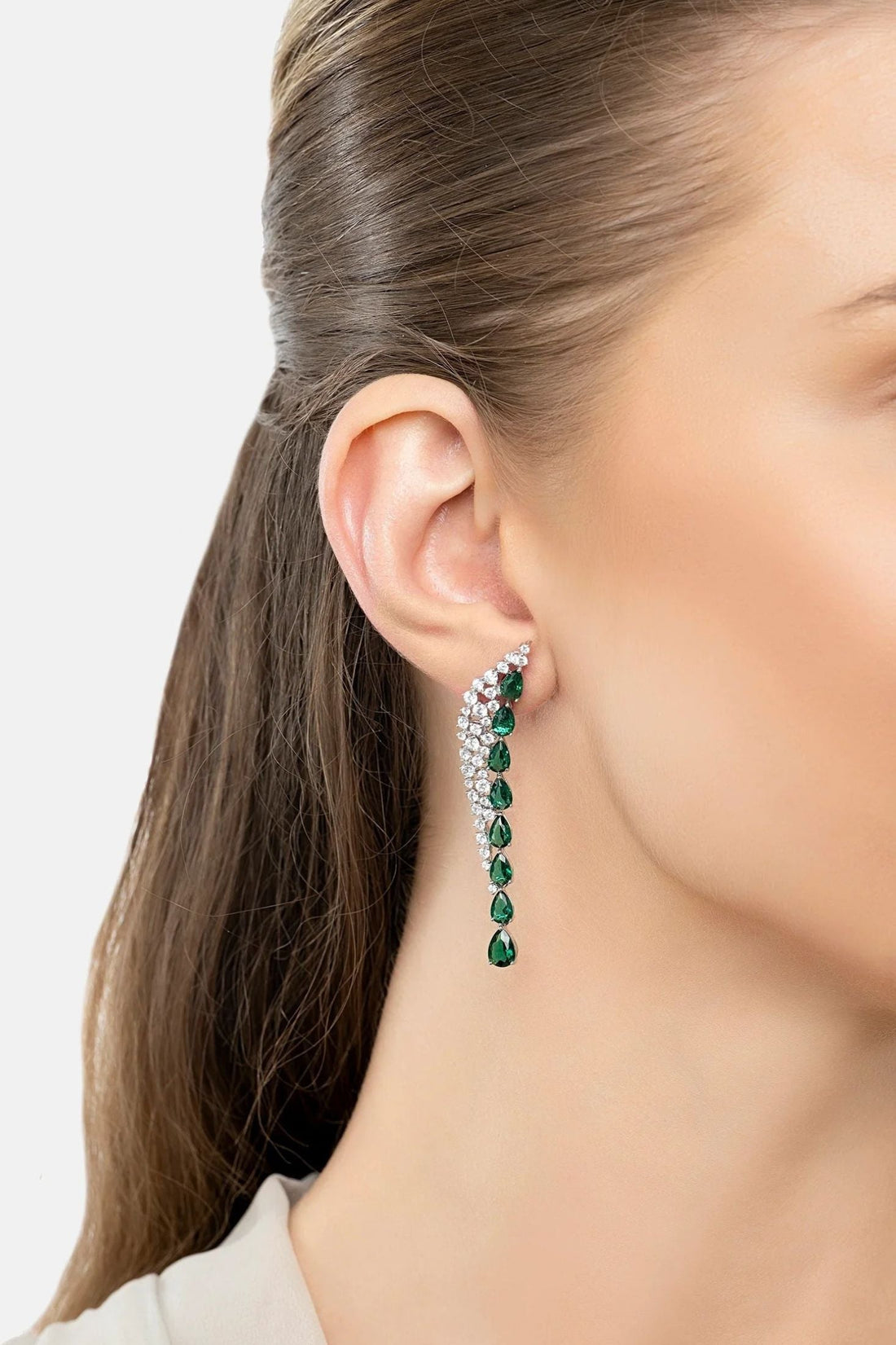 Model wearing gold-tone emerald green drop earrings with dangling gemstone row