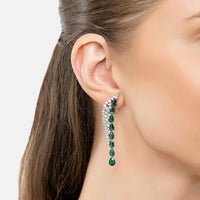 Model wearing gold-tone emerald green drop earrings with dangling gemstone row