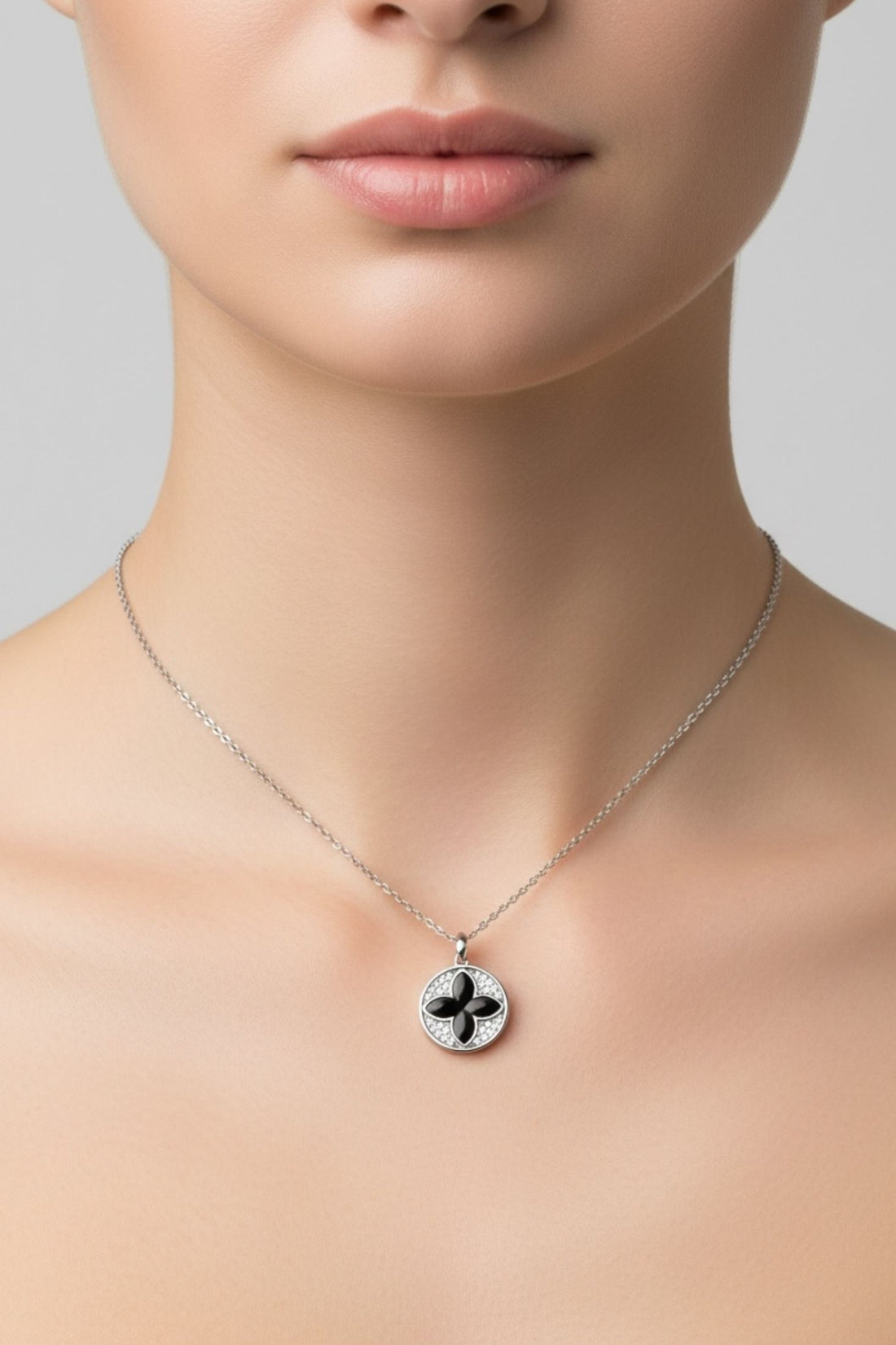 Silver chain necklace with small round pendant featuring black four-leaf clover center