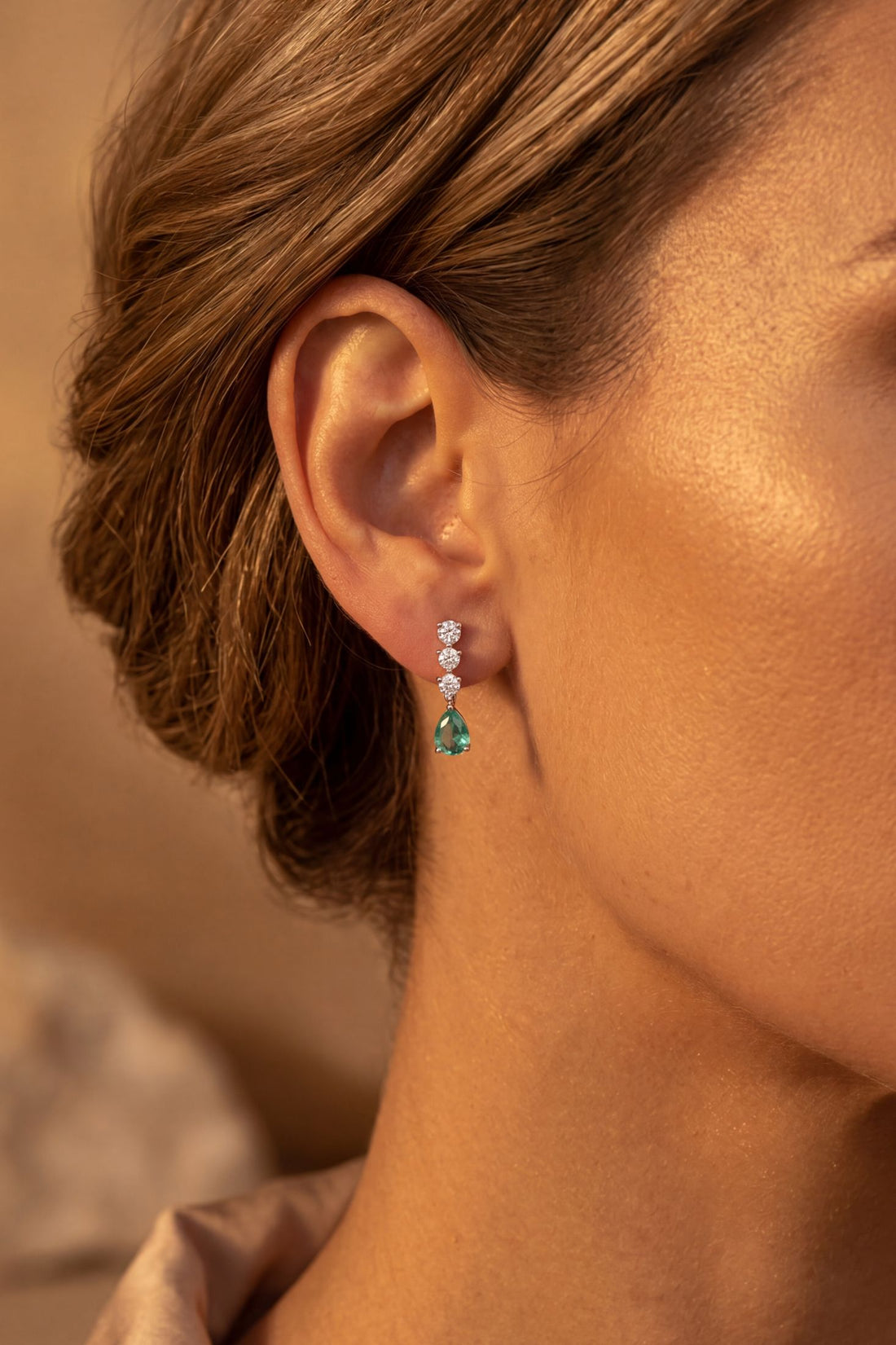 Silver drop earrings on ear with teal pear-shaped stone and tiny crystal stud