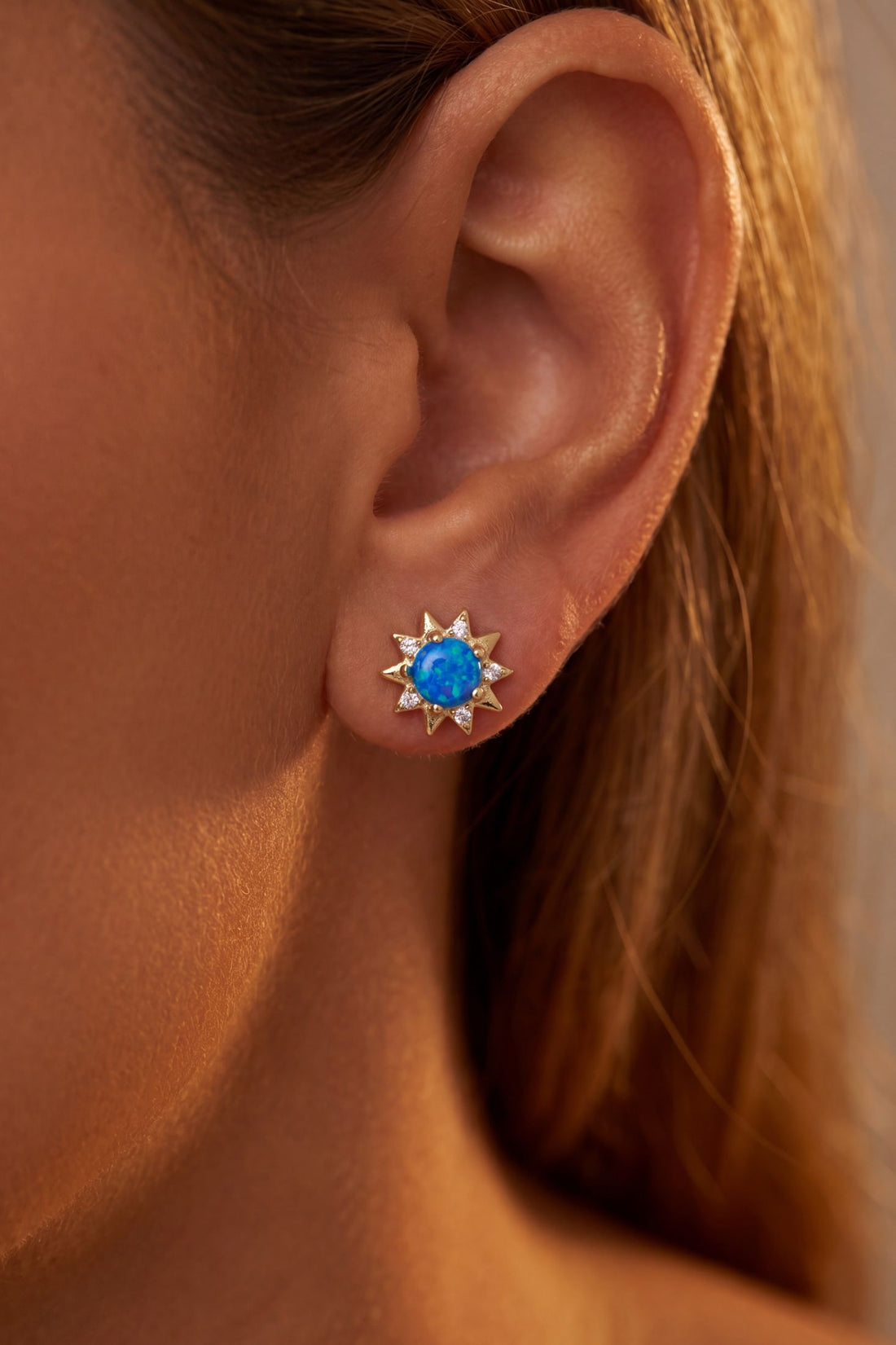 Gold sunflower blue opal stud earrings on ear with starburst crystal setting