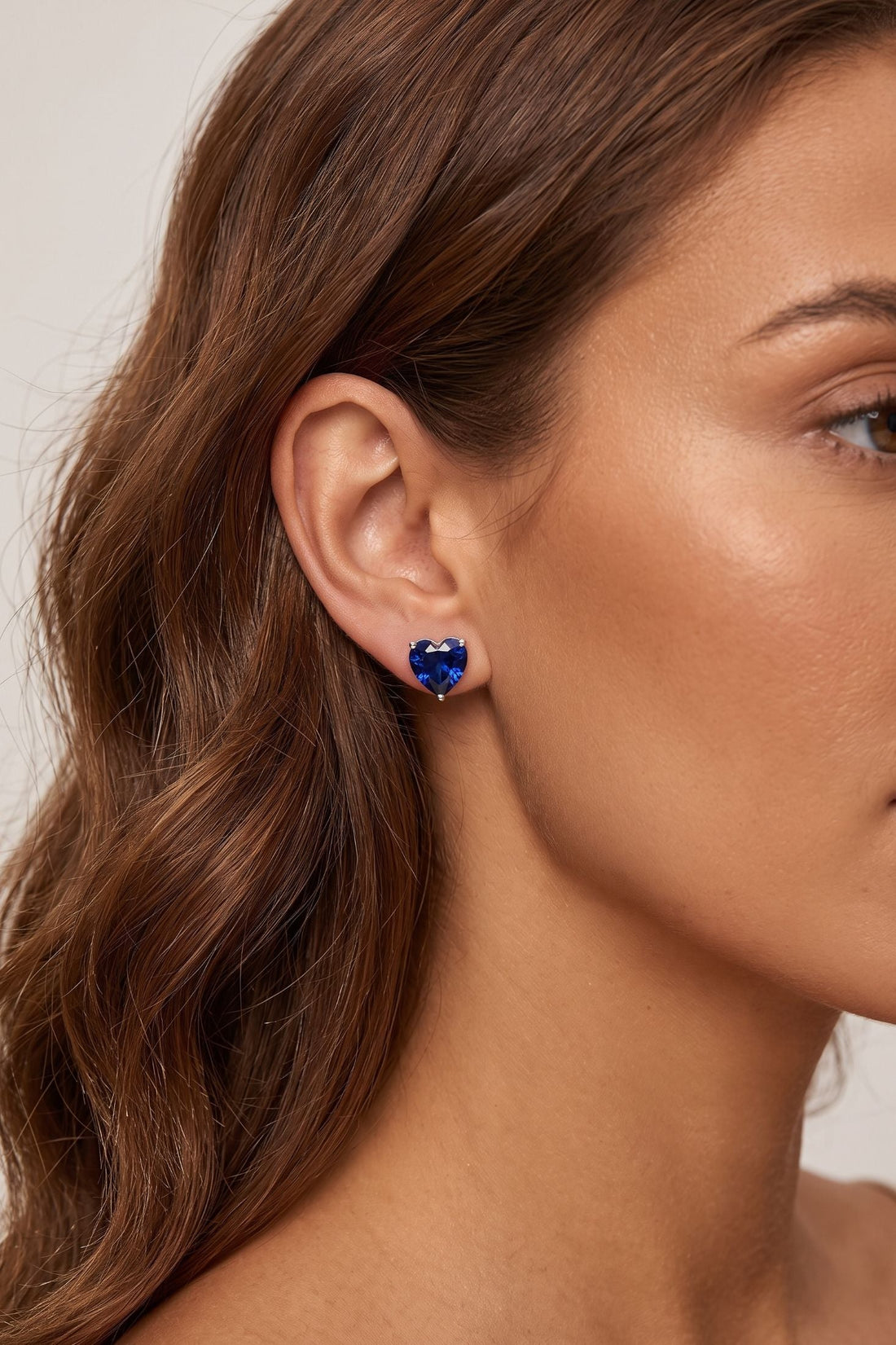 Heart-shaped sapphire-blue stud earring on ear with silver back