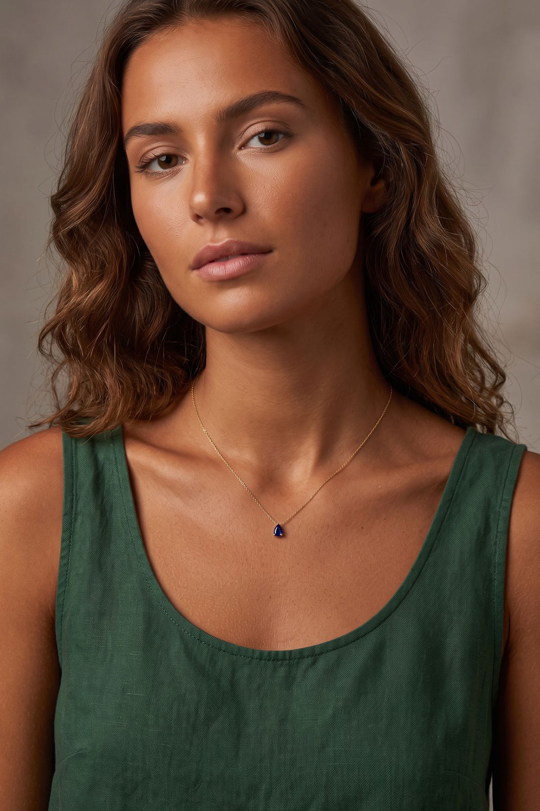 Gold teardrop necklace with blue gemstone pendant worn at neckline