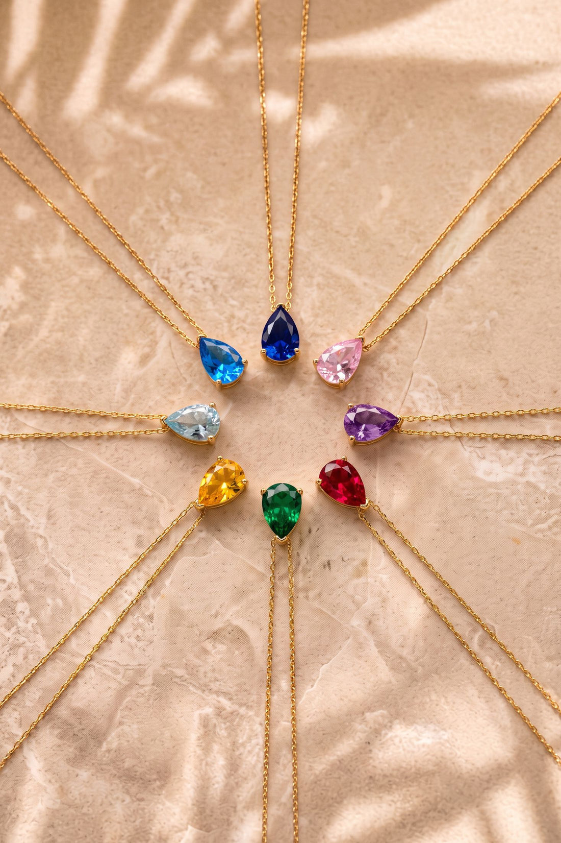 Gold teardrop gemstone pendants on chains, featuring purple, blue, and pink stones