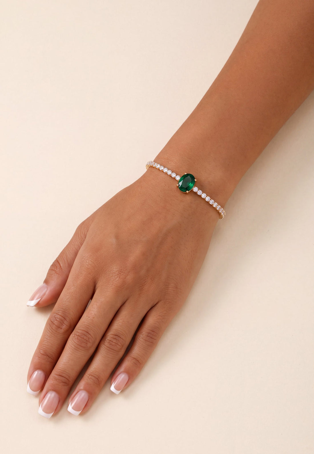 Garbo oval emerald tennis bracelet with gold setting and clear stones on wrist